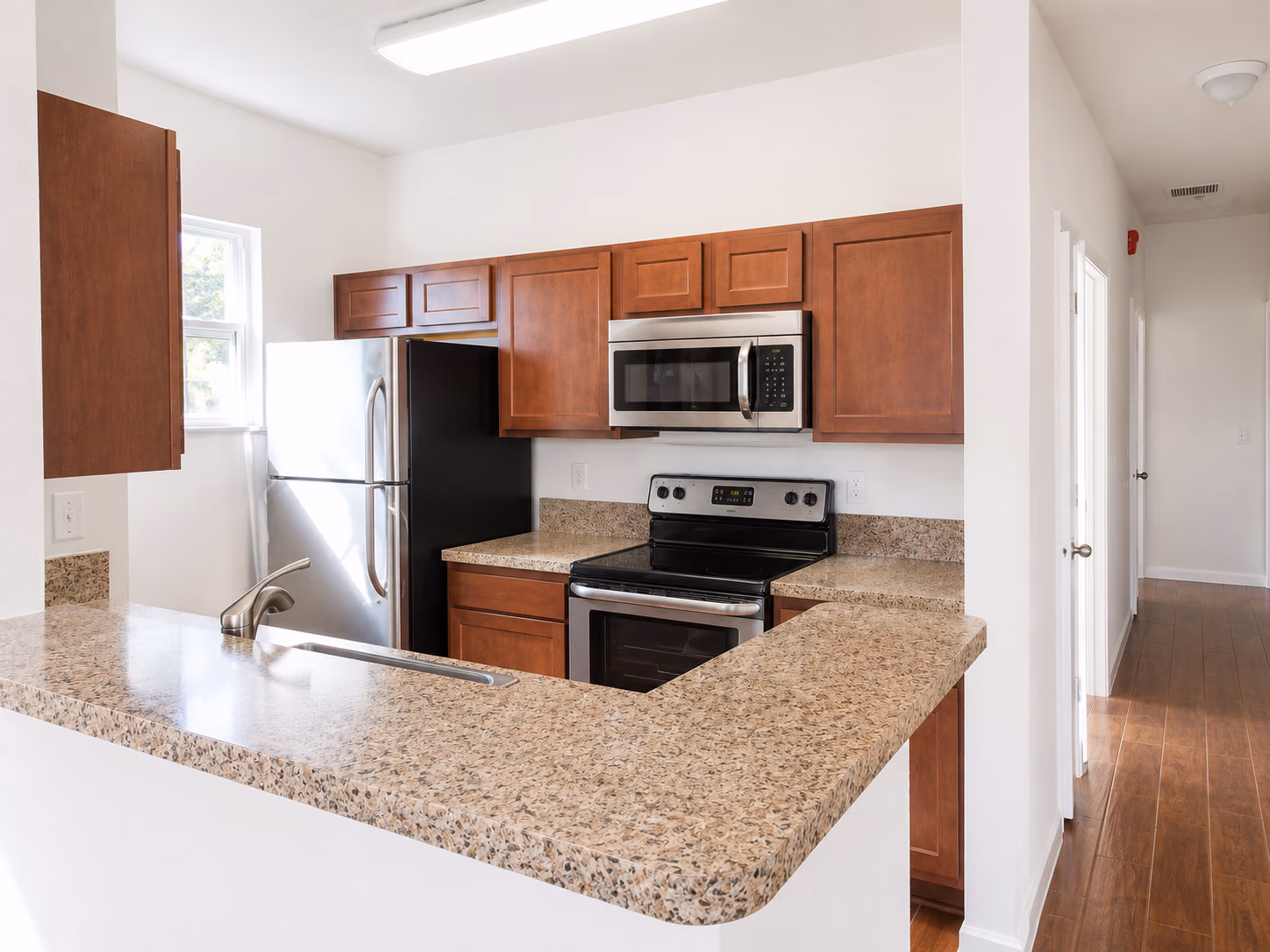 Modern kitchen with granite countertops, wooden cabinets, stainless steel fridge, stove, and microwave.