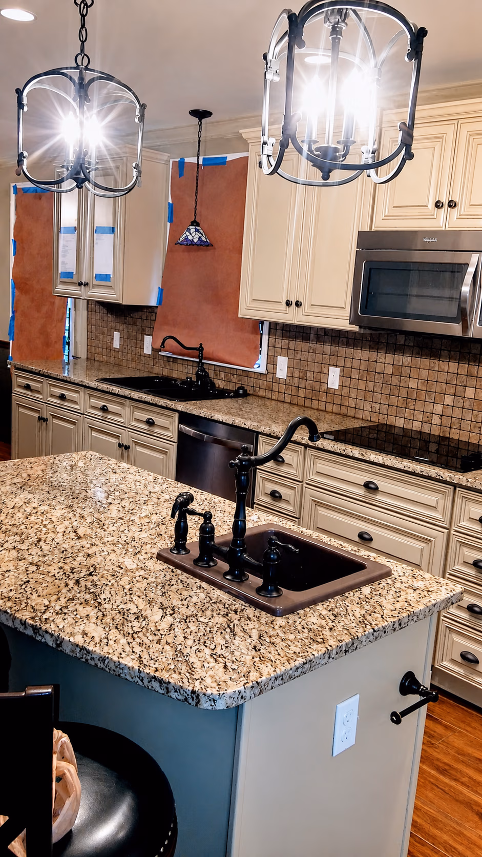 Modern kitchen with granite countertops, cream cabinets, black fixtures, and hanging light fixtures.