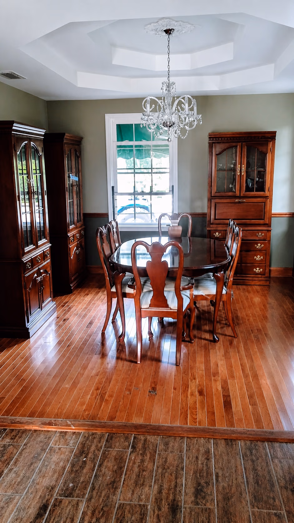 Traditional dining room with wooden table, chairs, cabinets, chandelier, and hardwood floor.