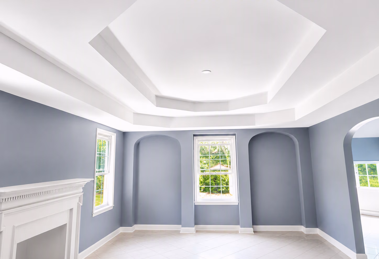 Empty room with gray walls, white tray ceiling, large windows, white fireplace, and tiled floor.