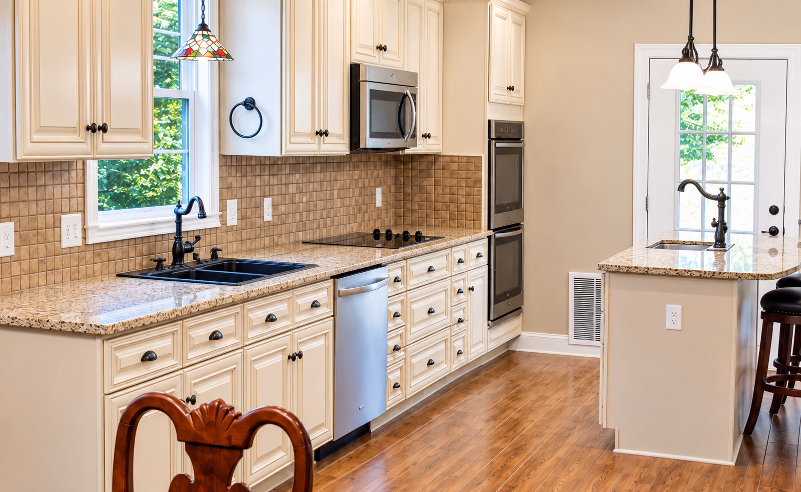 Kitchen with cream raised-panel cabinets, granite counters, a tile backsplash, double wall ovens and an island with a bar sink